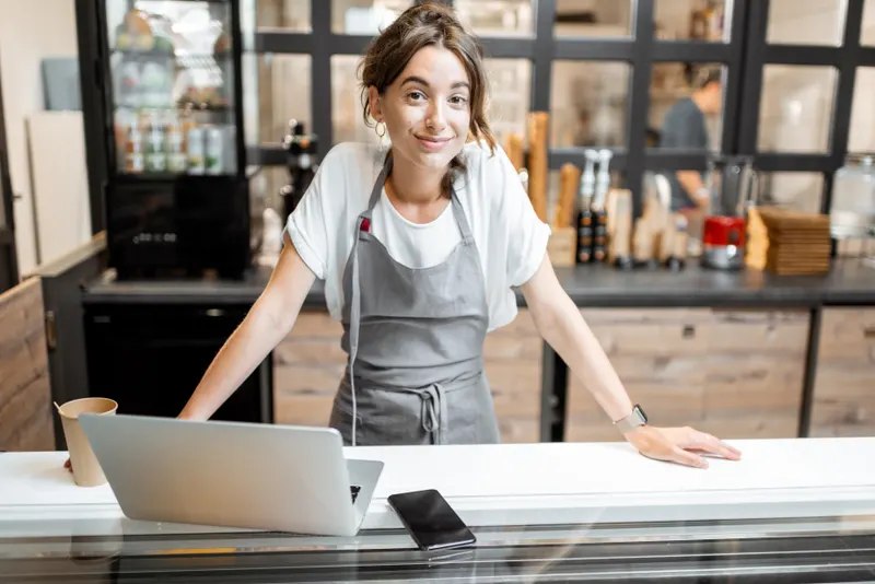 Une commerçante travaille sur son ordinateur portable derrière son comptoir.